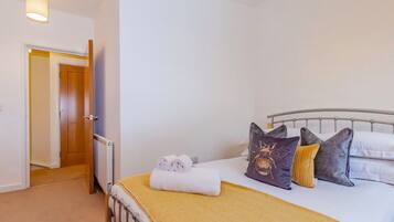 A bedroom with a bed, pillows, a rolled towel, a radiator, and a door leading to another room.