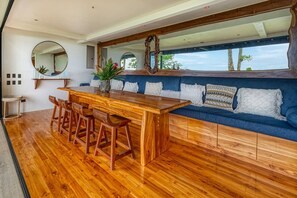 A wooden bar area with stools, a blue sofa with patterned cushions, and a large mirror. - Bali Villa Jungle Paradise by Pura Villas (Bahía Ballena)