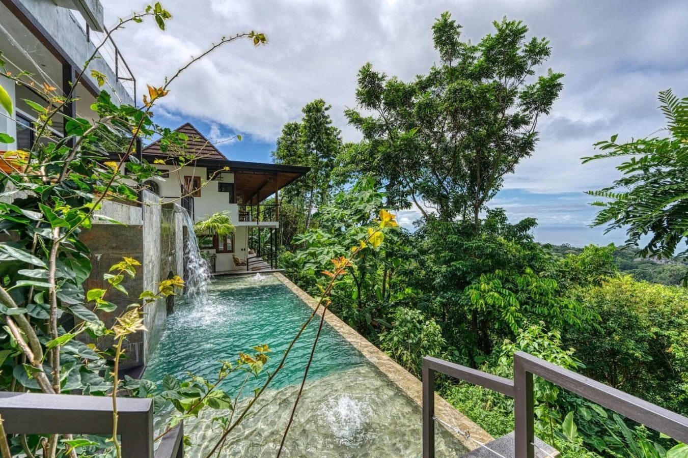 A modern house with a swimming pool, surrounded by lush greenery and a waterfall feature.