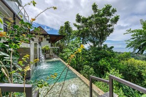 Una casa moderna con piscina, rodeada de exuberante vegetación y una cascada.