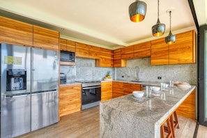 Una cocina moderna con armarios de madera, electrodomésticos de acero inoxidable, encimeras de granito e iluminación colgante.