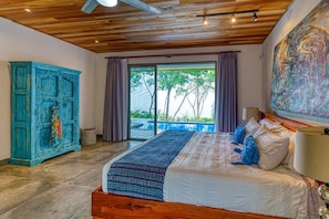 A bedroom with a large bed, a blue cabinet, and a view of a swimming pool. - Miralago Villa by Pura Villas (Bahía Ballena)