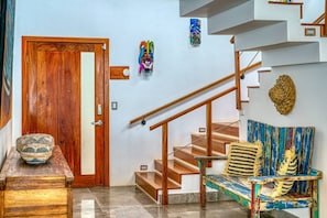 Uma porta de madeira com uma placa, uma escadaria com corrimão e um banco com almofadas coloridas.