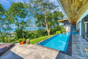 A modern pool area with a view of the ocean, surrounded by lush greenery and a wooden deck. - Miralago Villa by Pura Villas (Bahía Ballena)