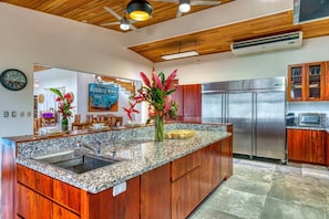 A modern kitchen with granite countertops, wooden cabinets, a stainless steel refrigerator, and a ceiling fan. - Miralago Villa by Pura Villas (Bahía Ballena)