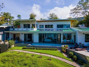 Uma casa moderna de dois andares com piscina, painéis solares e um jardim bem cuidado.