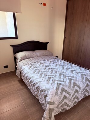 A bedroom with a bed, a wooden door, and a window with blinds. - New 2BR Apt with A/C & Pool Access, Downtown Cartago (Cartago)