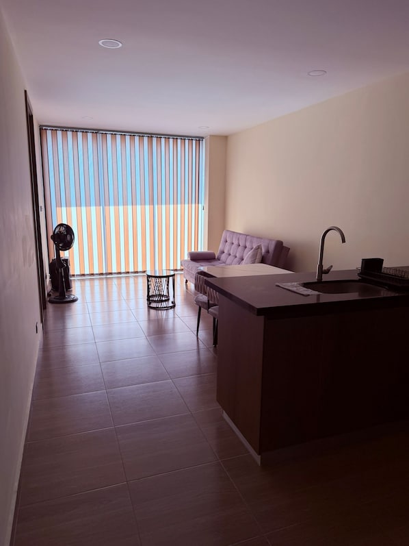 A modern kitchen with a central island, a dining area with a sofa, and a large window with blinds. - New 2BR Apt with A/C & Pool Access, Downtown Cartago (Cartago)