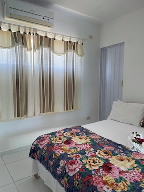 A hotel room with a bed, a window with curtains, a wall-mounted air conditioner, and a door. - New Listing (Japaratinga)