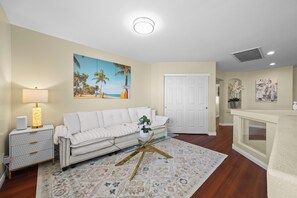 A living room with a white sofa, a lamp, a painting of a beach, and a patterned rug. - Vegas Luxe Retreat Pool, Pool Table, Near Strip (Las Vegas)
