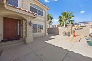 A two-story house with a red door, large windows, and a patio area with chairs and planters. - Vegas Luxe Retreat Pool, Pool Table, Near Strip (Las Vegas)