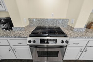 A kitchen with a stainless steel stove, granite countertop, and white cabinetry. - Vegas Luxe Retreat Pool, Pool Table, Near Strip (Las Vegas)