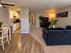 A modern living room with a dark sofa, a kitchen area with white cabinets, and a dining table with chairs. - Walking distance to AT&T Stadium and the entertainment district, FREE parking (Arlington)