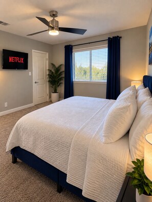 A bedroom with a bed, a ceiling fan, a TV displaying 'NETFLIX,' a window with curtains, and a potted plant. - Walking distance to AT&T Stadium and the entertainment district, FREE parking (Arlington)