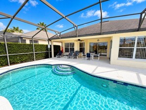 A swimming pool with a covered patio area, lounge chairs, and a clear blue sky. - The Sunset Retreat - Close to Disney World (Davenport)
