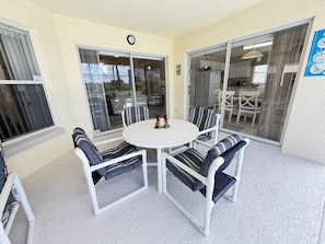 Un patio couvert avec une table ronde et quatre chaises, une horloge au mur et une vue sur la cuisine adjacente.