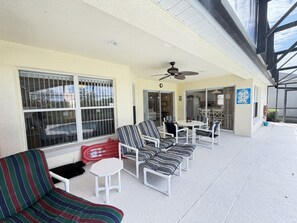 A covered outdoor seating area with chairs and tables, a ceiling fan, and a view of the street through large windows. - The Sunset Retreat - Close to Disney World (Davenport)