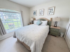 Une chambre à coucher avec un lit, une table de chevet, une lampe et une fenêtre avec des rideaux.
