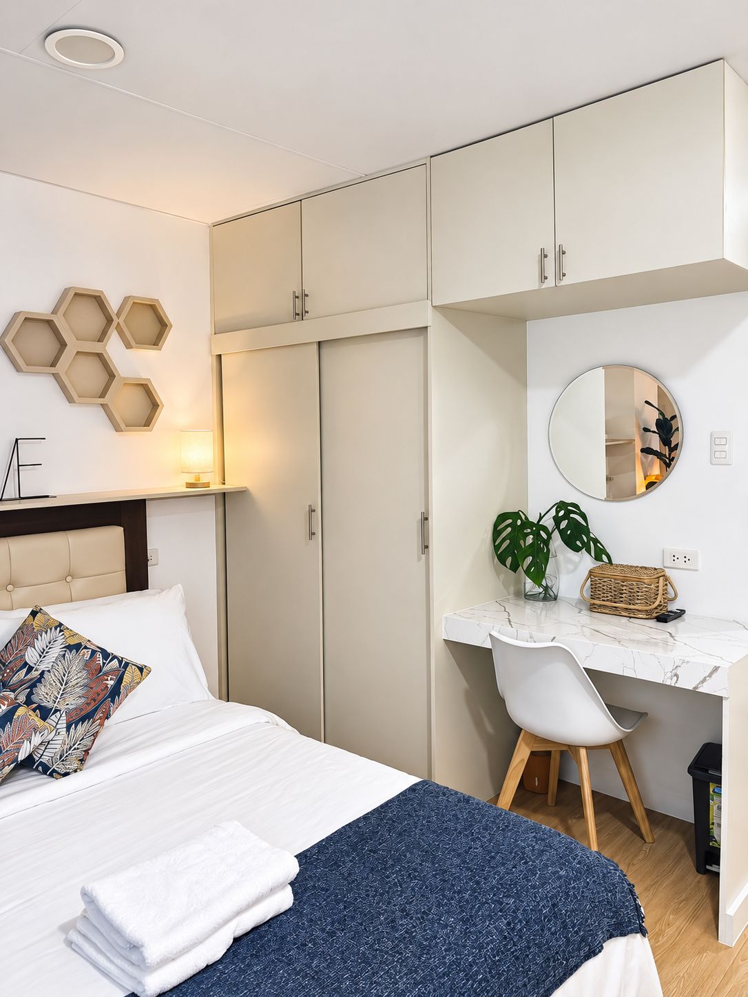 Een slaapkamer met een bed, een bureau, een stoel, een kledingkast en een spiegel aan de muur.