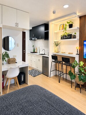 Een moderne keuken met witte kasten, een zwart aanrecht en een inbouwoven. Twee zwarte barkrukken en een kleine eettafel met een zwart-wit vloerkleed.