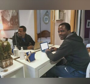 A room with two individuals seated at a desk with laptops, a small plant, and a bottle of hand sanitizer. - City Gateway Home W/Self Check-In (L'Hospitalet de Llobregat)
