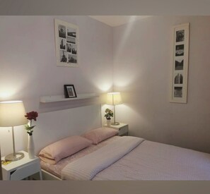 Een slaapkamer met een bed, twee nachtkastjes, een wandplank en ingelijste foto's.