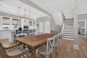 A spacious kitchen with a dining area, white cabinetry, and a wooden staircase. - BayGlass Cove | Beachfront home in Bay Creek (Cape Charles)