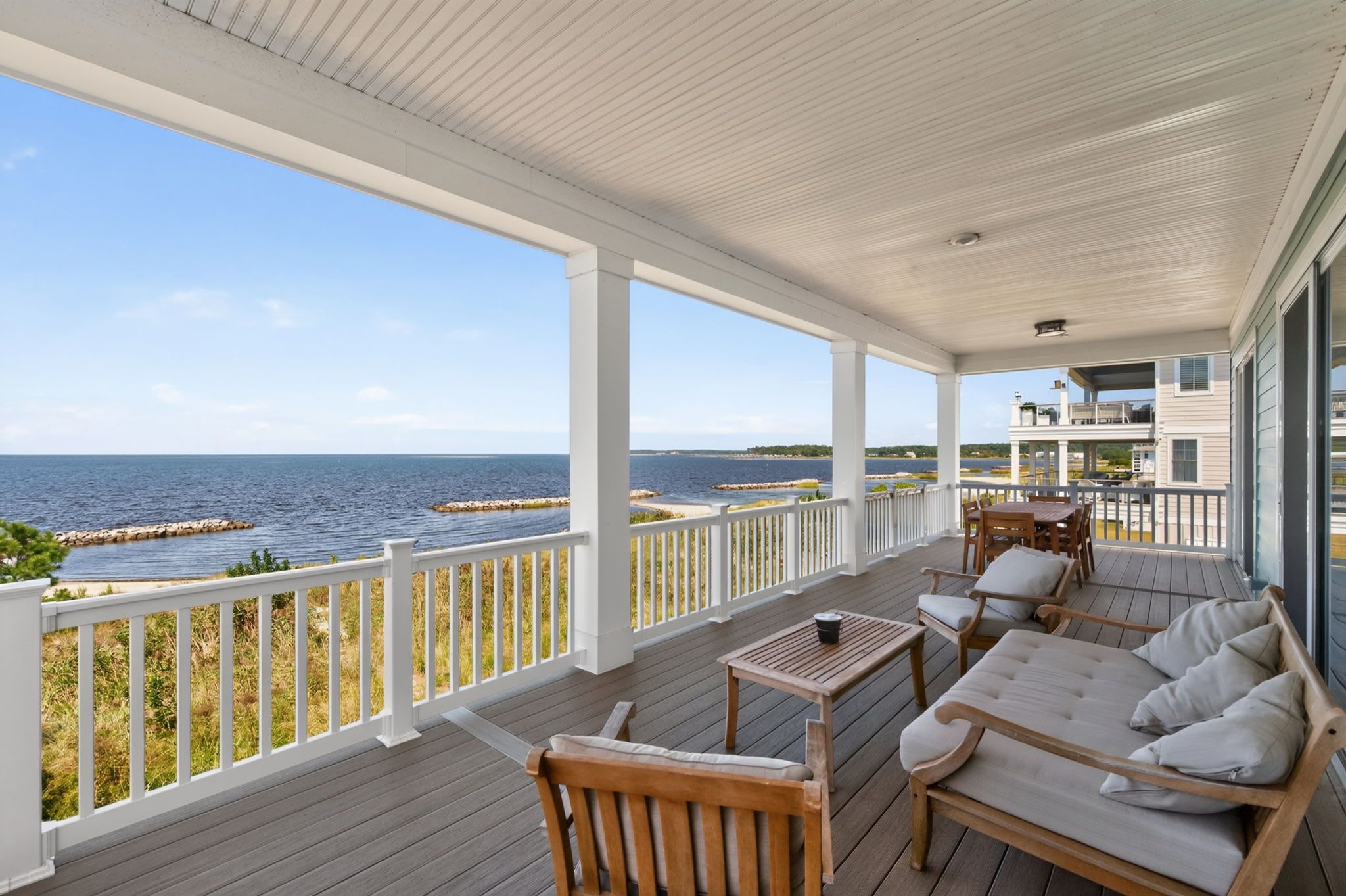 A covered porch with a view of the sea, wooden furniture, and a railing.