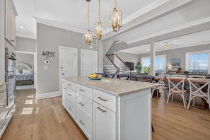 A spacious kitchen with a central island, wooden flooring, and pendant lighting. - BayGlass Cove | Beachfront home in Bay Creek (Cape Charles)