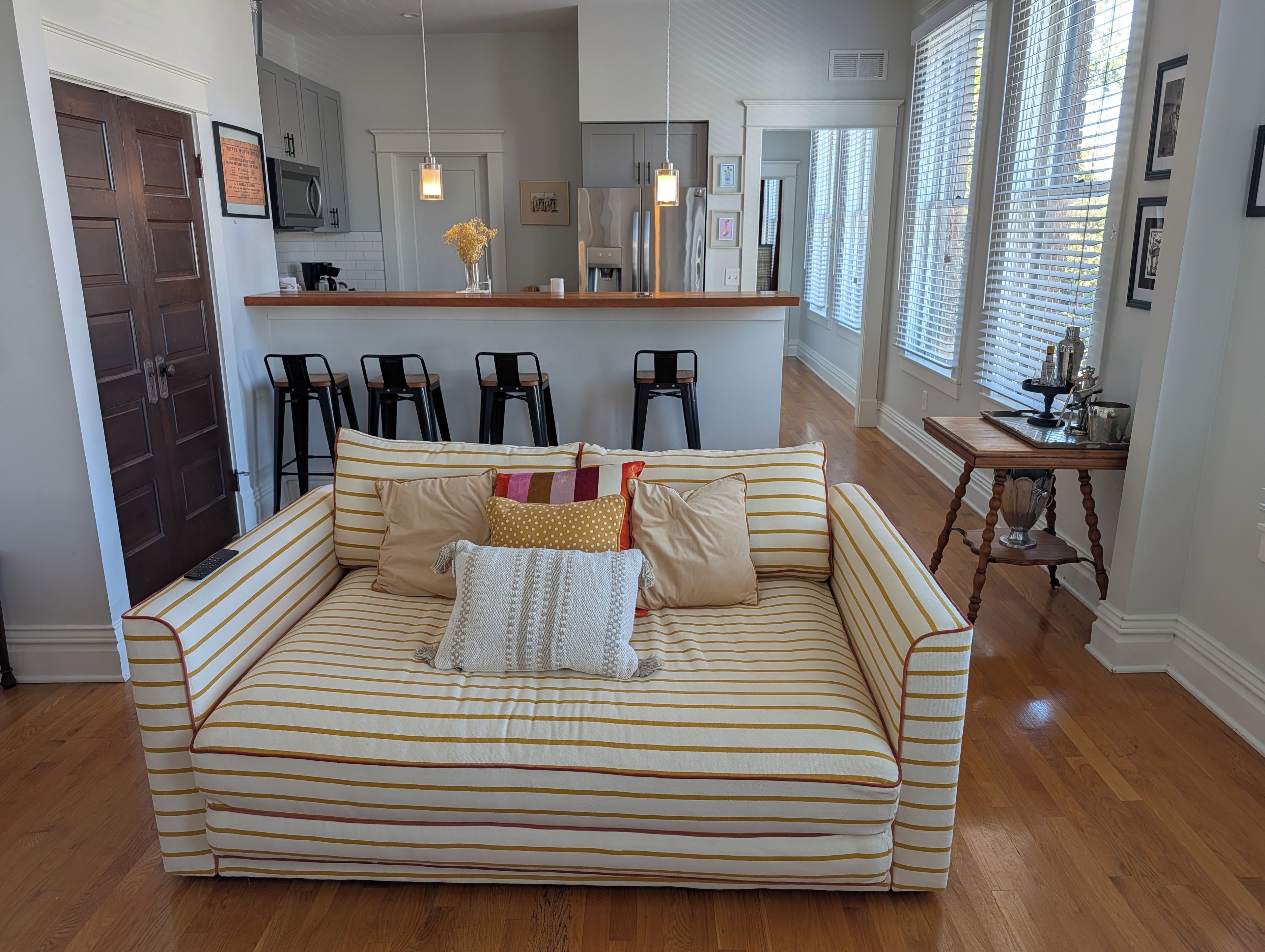 Een moderne woonkamer met een gestreept bankje, een bijzettafeltje en een keuken op de achtergrond.