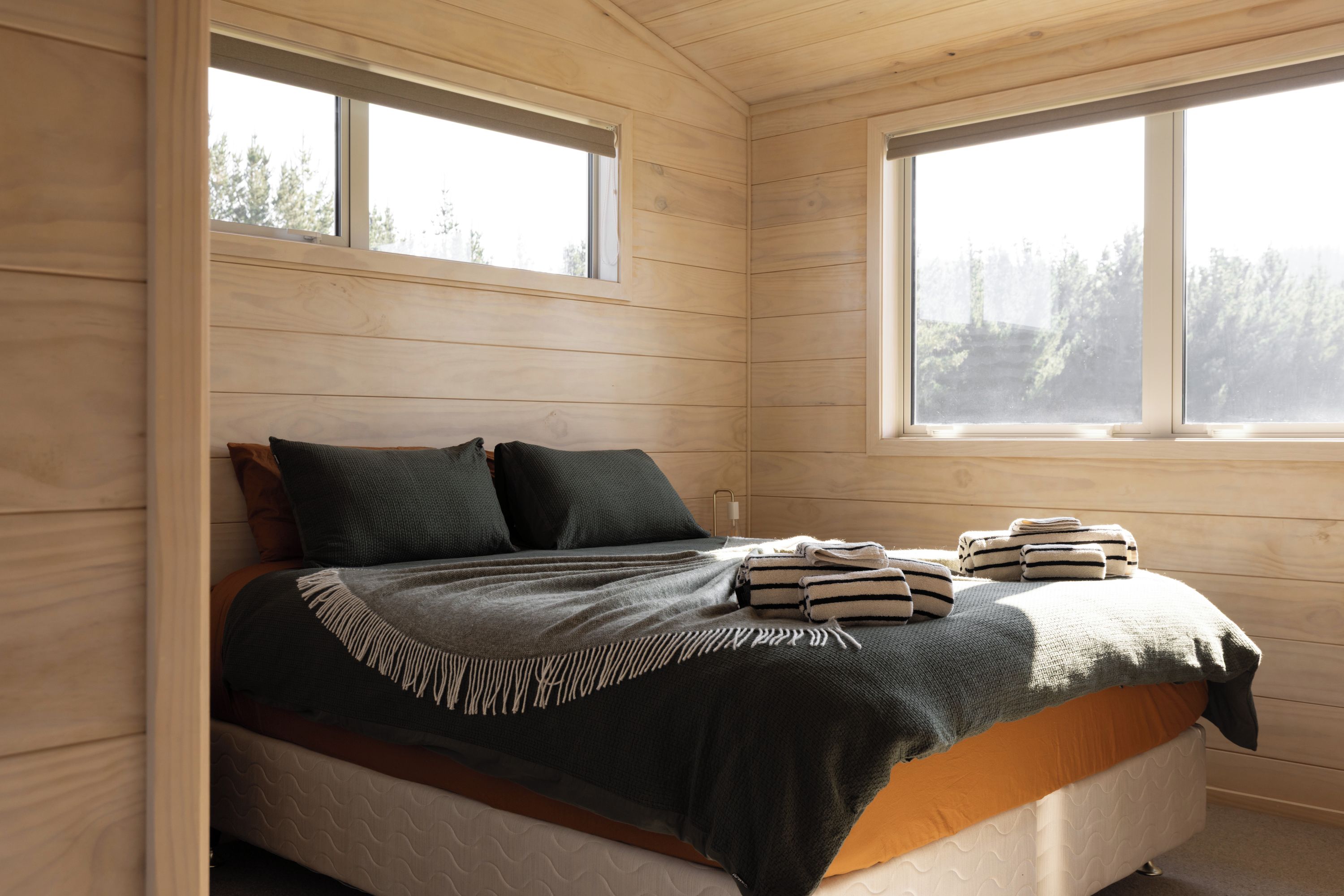 A wooden cabin bedroom with a bed, pillows, and a window.