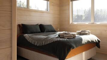 A wooden cabin bedroom with a bed, pillows, and a window.