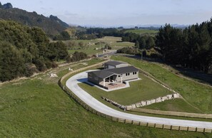 A modern two-story building with a covered patio, surrounded by a fenced property and a curving road. - Rural retreat close to Rotorua tourist attractions, Hot Pools & Thermal areas (Ngakuru)
