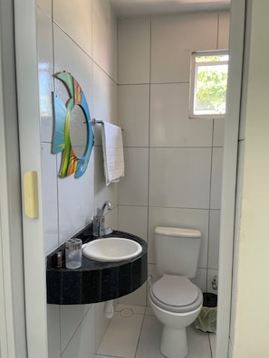 A bathroom with a white toilet, a sink with a black countertop, and a window with a view of greenery. - New Listing (Japaratinga)