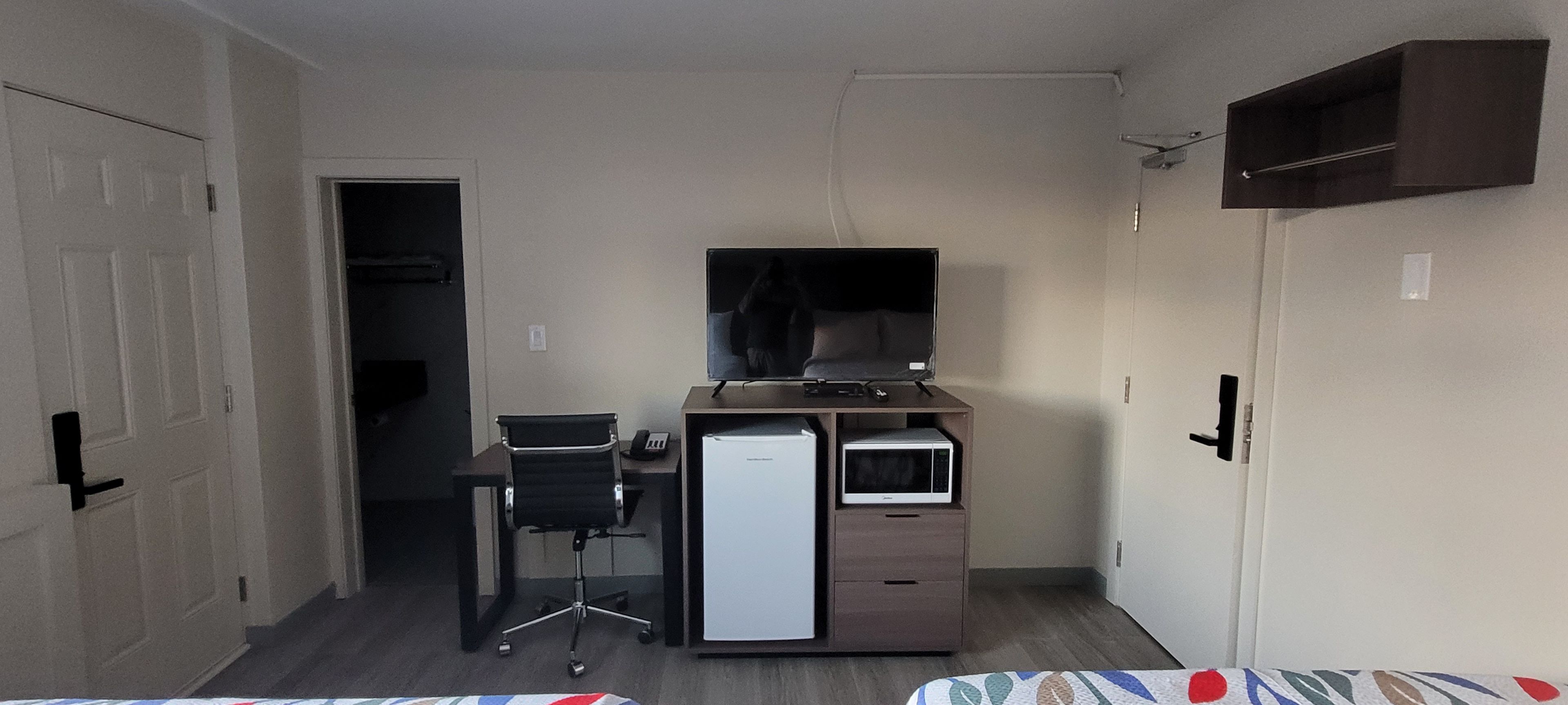 Une pièce de taille modeste, comprenant un bureau, une chaise, un téléviseur et une armoire.