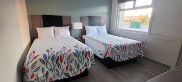 Habitación de hotel con dos camas, cada una con una colcha estampada, una mesita de noche con lámpara y una ventana con vistas al exterior.
