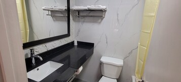 Un baño con encimera negra, lavamanos blanco, espejo y retrete.