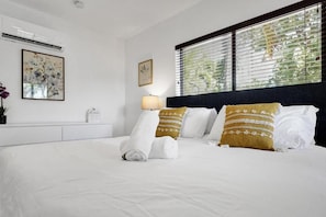 A hotel room with a bed, a nightstand, a lamp, and two windows with blinds.