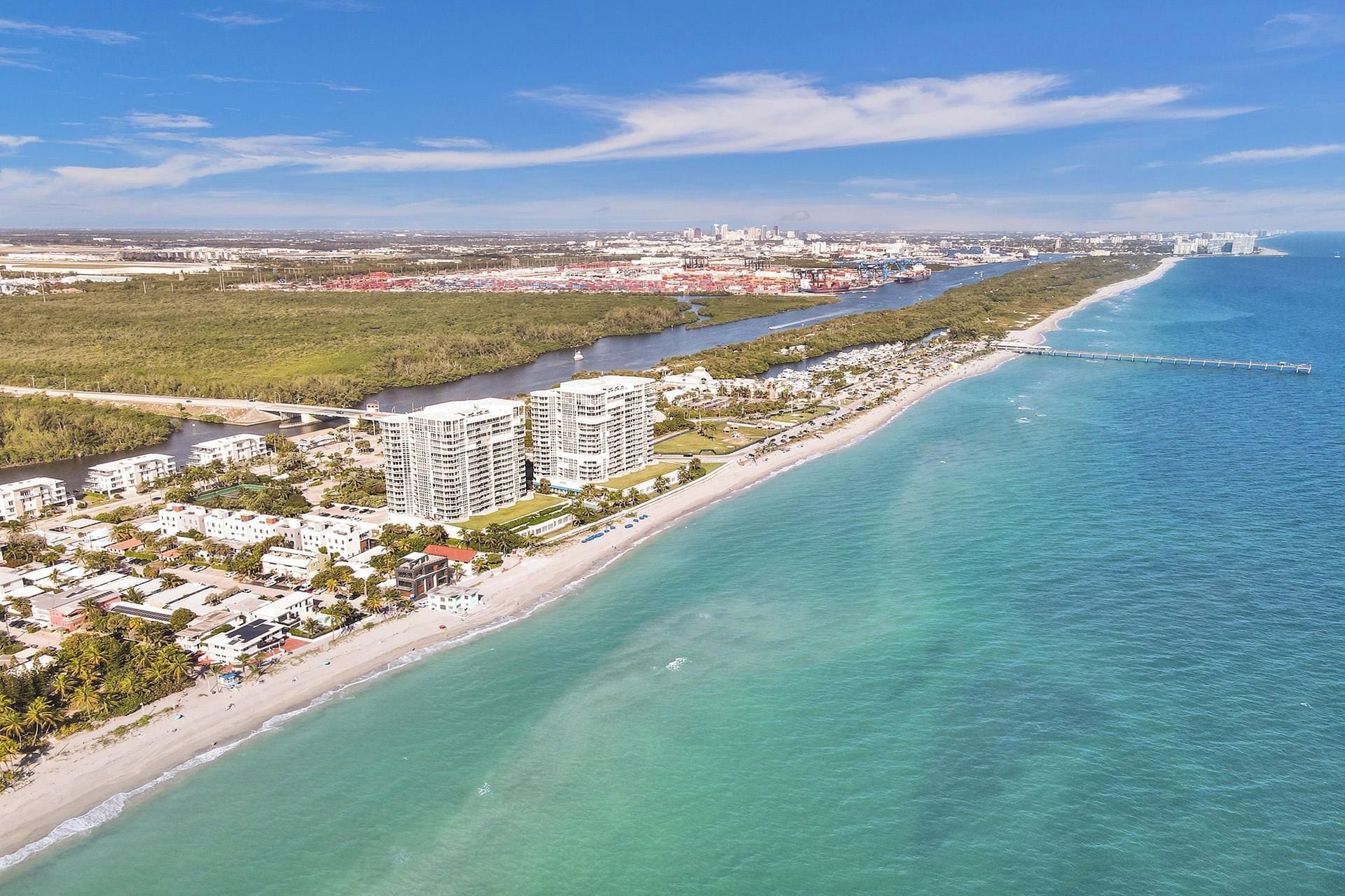 A coastal cityscape with a beachfront hotel, a marina, and a long pier extending into the water.