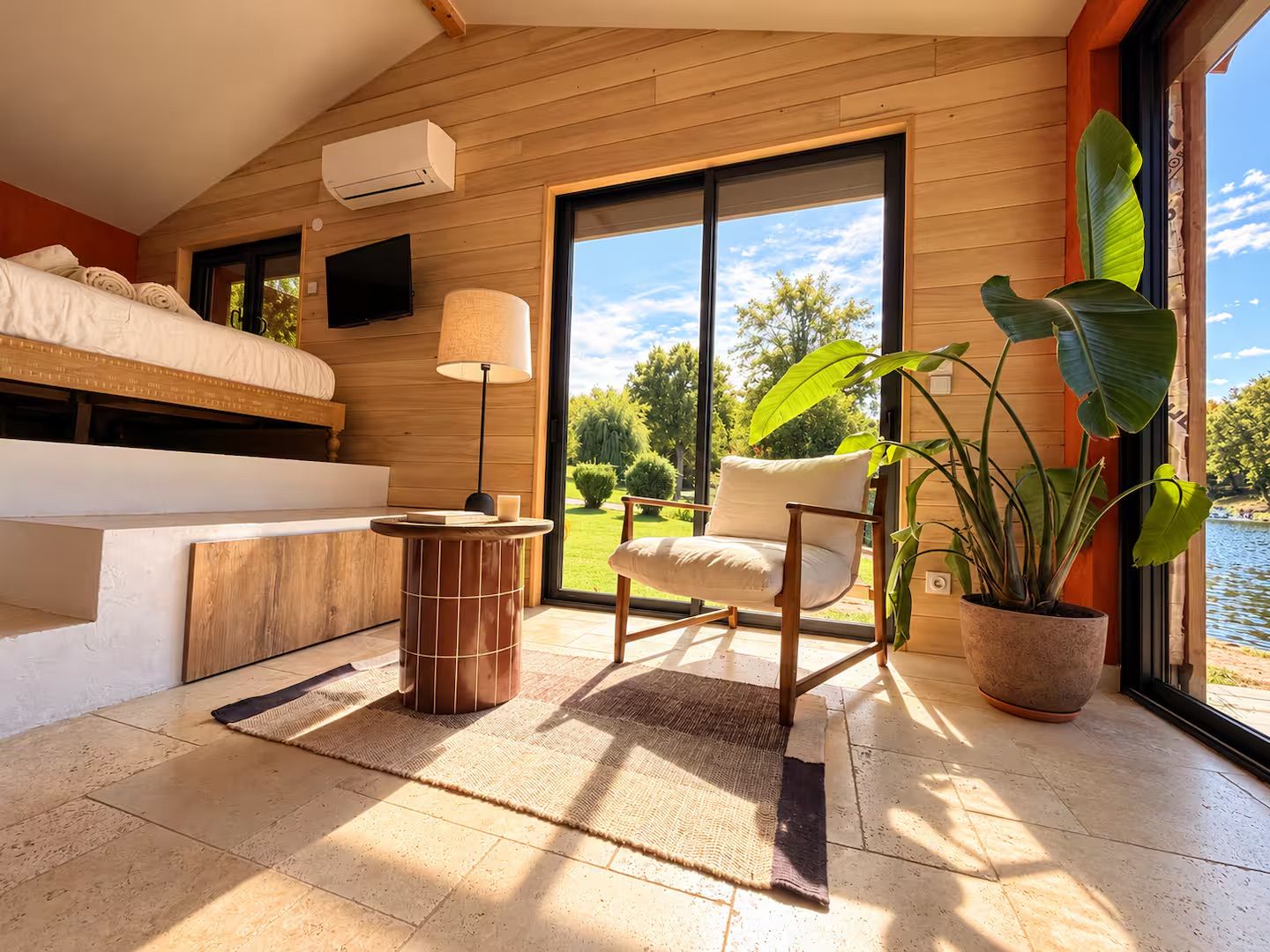 Un dormitorio con cama, televisión, ventana y vista a un jardín.