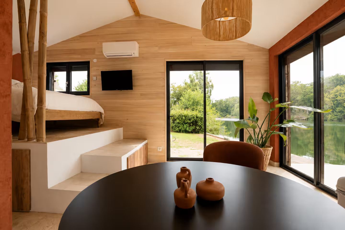 Una camera moderna con un letto, un tavolo da pranzo con ceramiche, una televisione e vista su un lago.