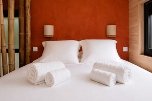 A hotel room with a bed, two pillows, two rolled towels, a wall with a textured pattern, and two wall-mounted lamps. - New Listing (Sainte-Livrade-sur-Lot)