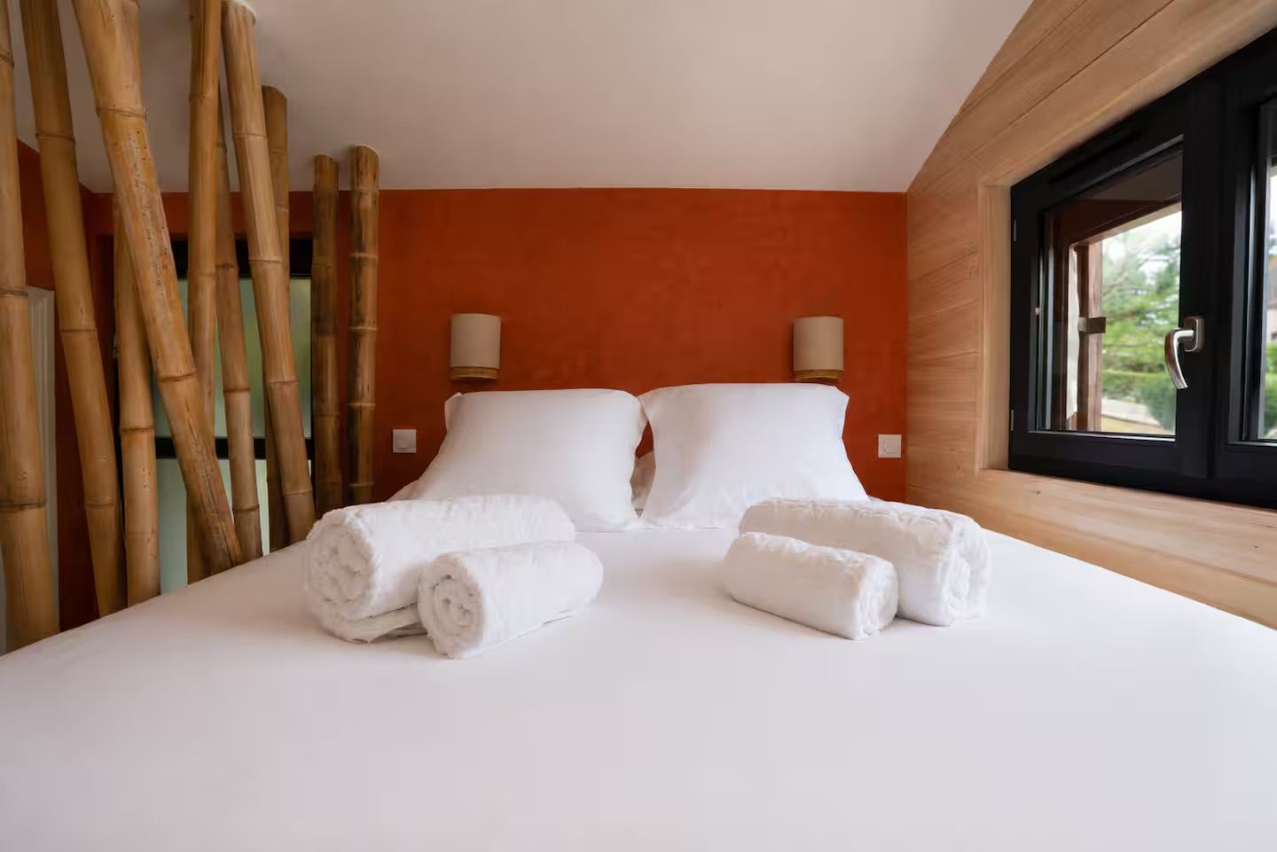 A hotel room with a bed, two pillows, two wall-mounted lamps, and a window with a view.