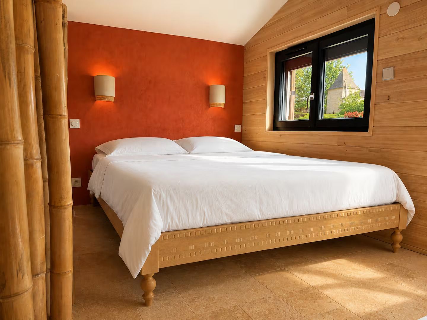 Une chambre à coucher avec un lit en bois, deux lampes fixées au mur et une fenêtre donnant sur un paysage verdoyant.