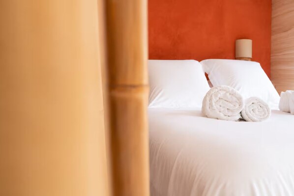 A hotel room with a neatly made bed, white linens, and rolled towels.