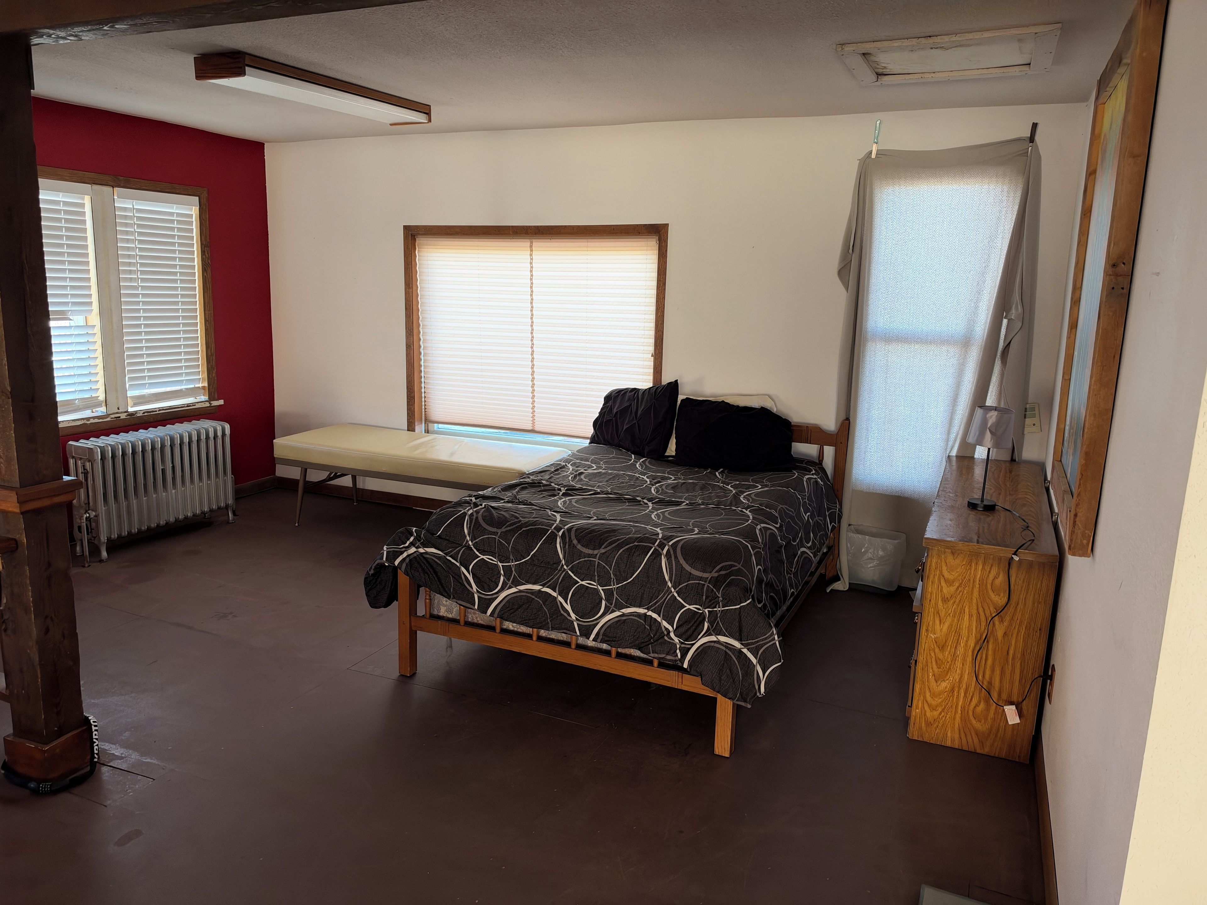 A bedroom with a bed, a bench, a radiator, a window, and a mirror.