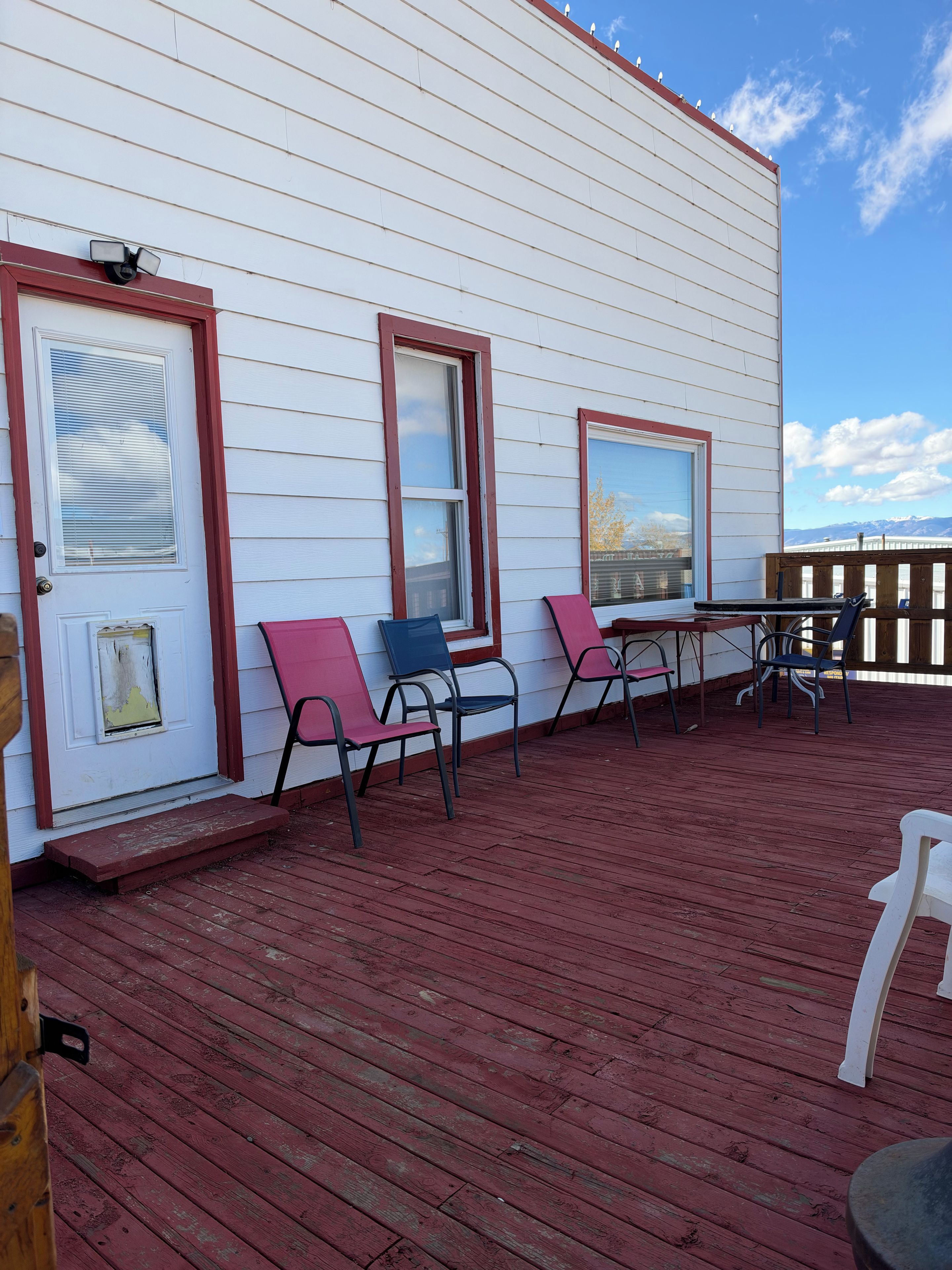 Un espace extérieur abrité, doté d’une terrasse en bois rouge, de murs blancs et offrant une vue sur les montagnes en arrière-plan.