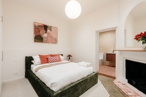 Ein Schlafzimmer mit einem Bett, einem Nachttisch, einer Lampe, einem Kamin und einem Bild an der Wand.