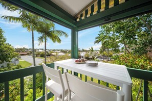 A balcony with a white table and chairs, overlooking a residential area with palm trees and houses. - The Breezy Abode - Dog-Friendly, Views & Deck (Caloundra Region)