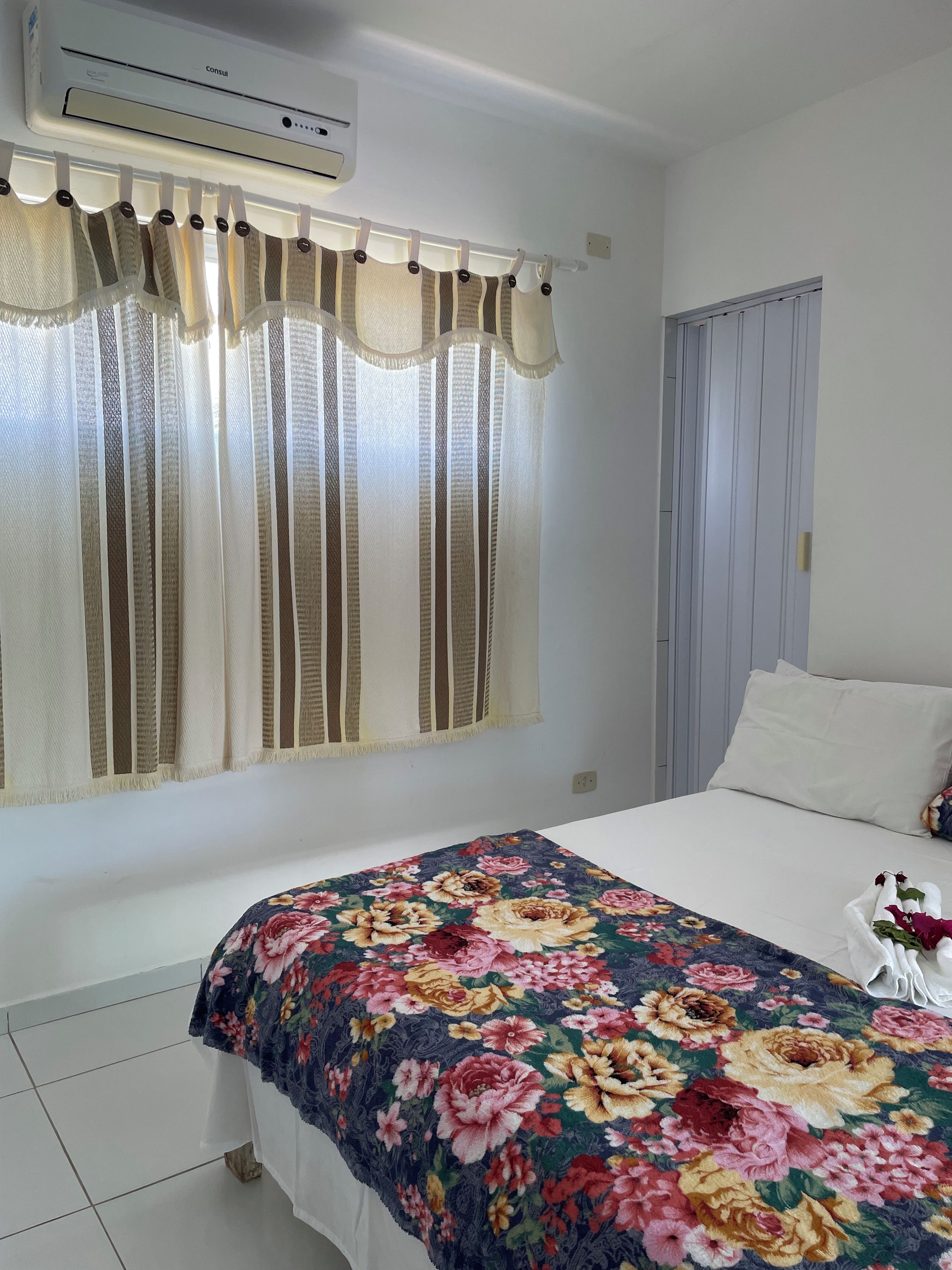 Une chambre d’hôtel avec un lit, une fenêtre avec des rideaux, un climatiseur fixé au mur et une porte.